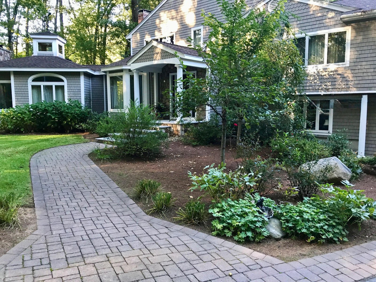 The same walkway edged clean, with fresh mulch beds and new plantings across the front of the house