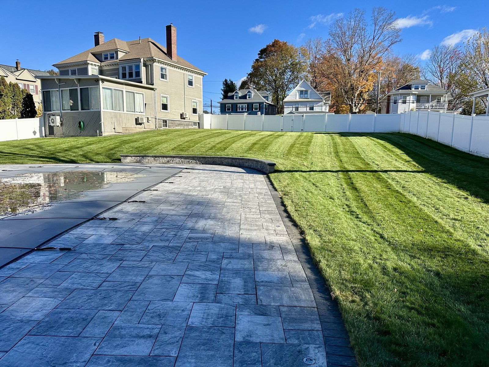 Large stamped concrete patio beside a freshly striped green lawn behind a New England home