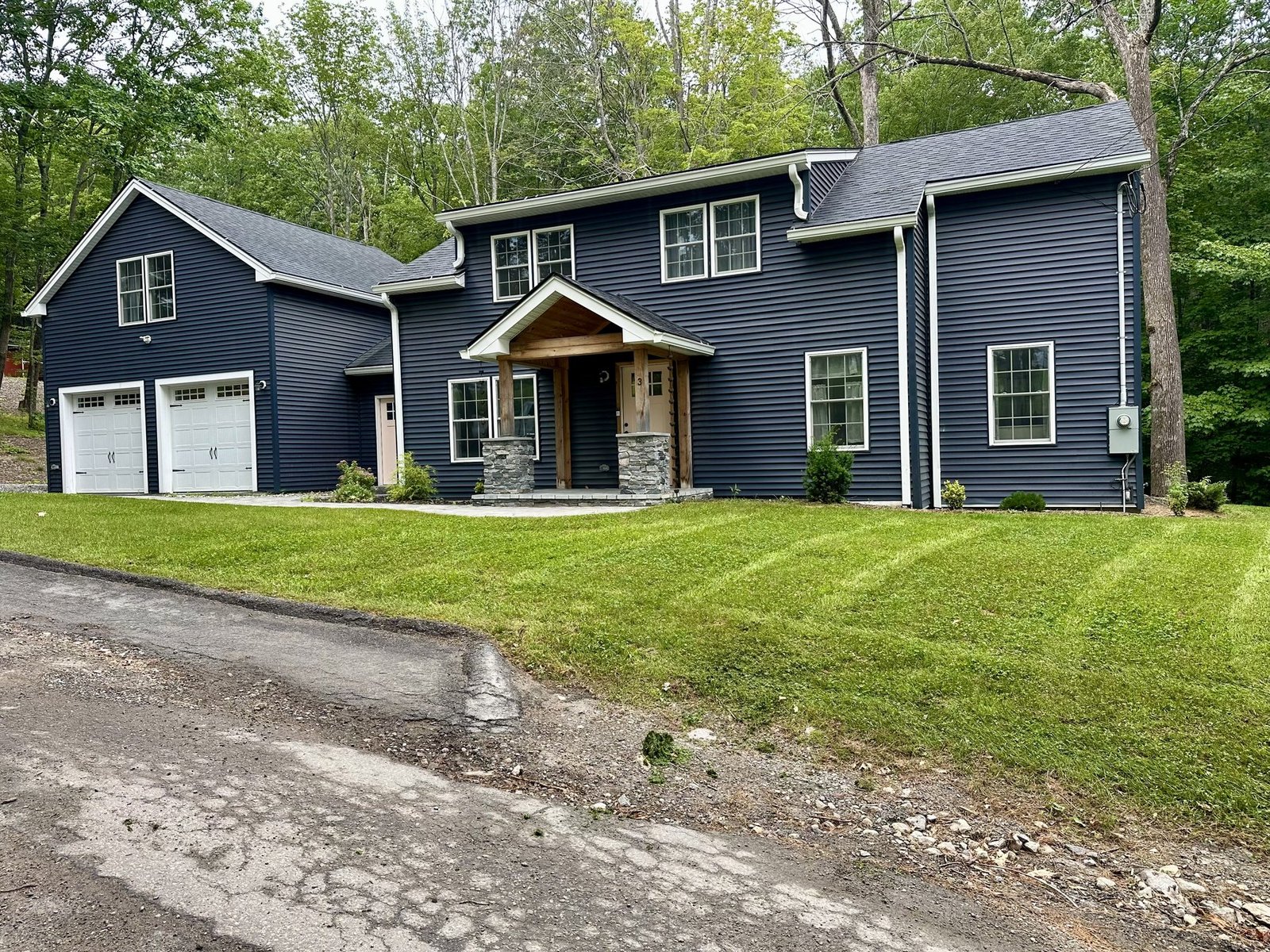 Navy blue colonial home with a freshly cut front lawn sloping down to the driveway