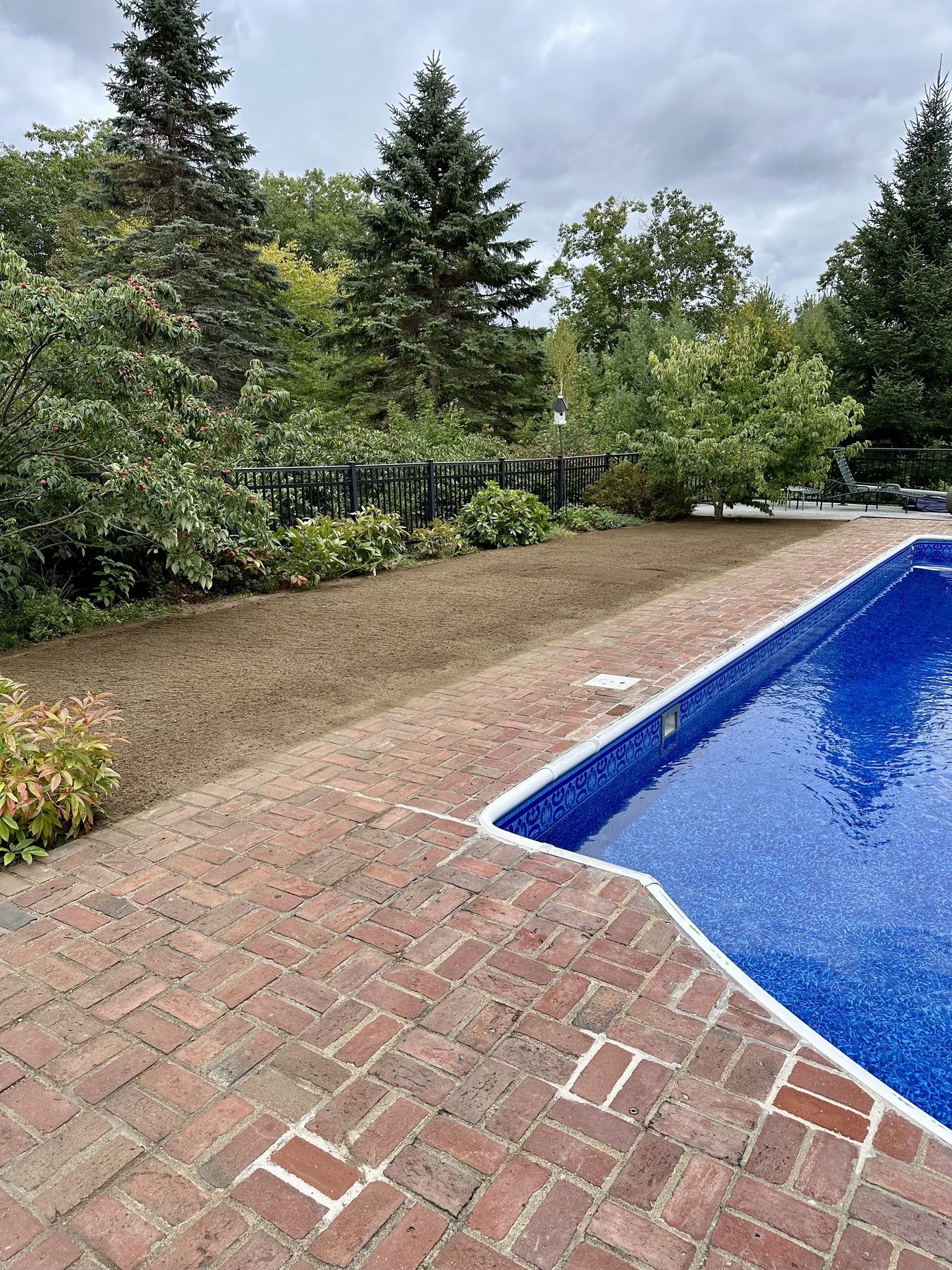 In-ground pool with a brick paver patio and a freshly loamed planting strip along the fence