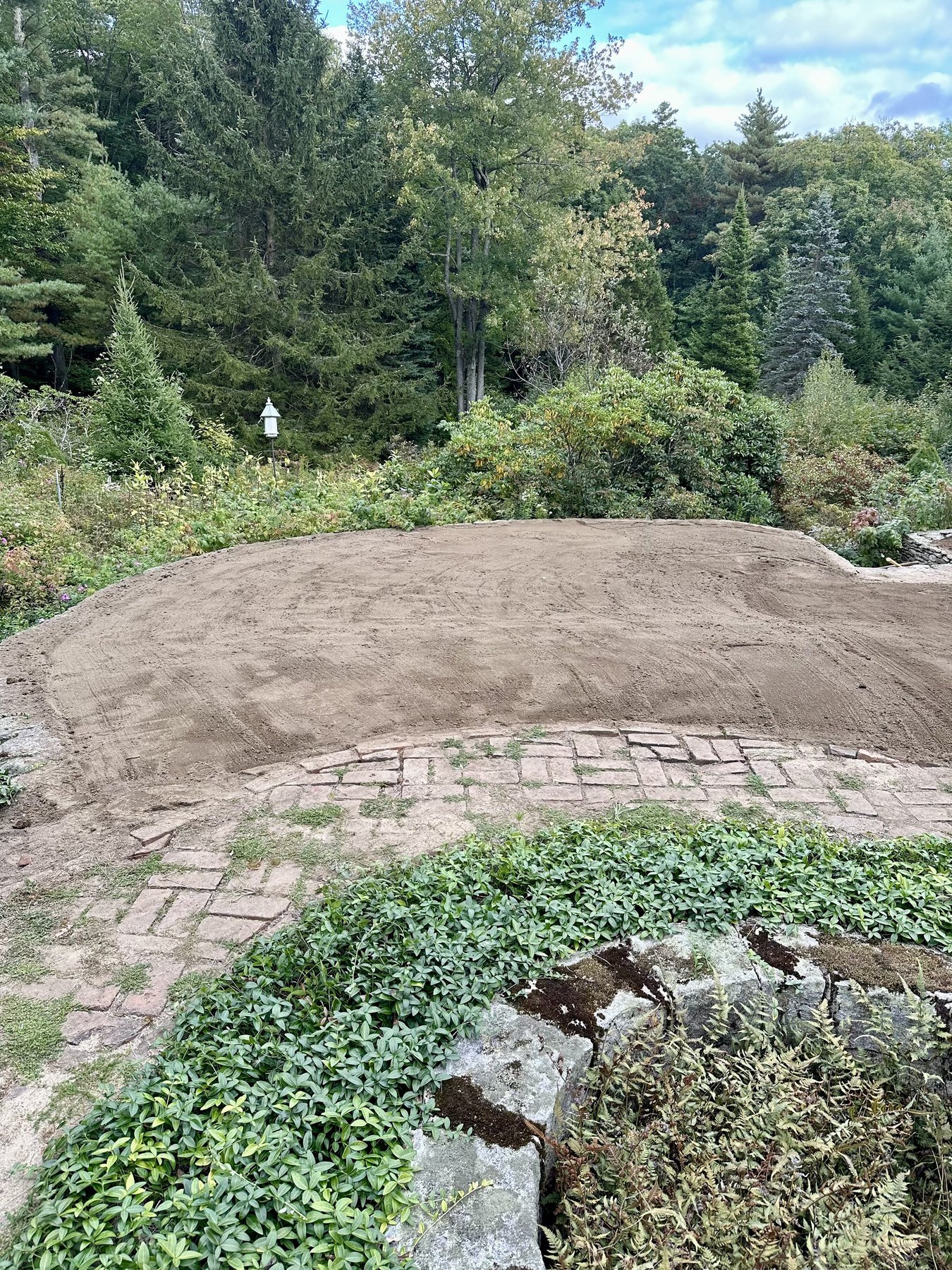 Graded and raked topsoil on a slope above a brick patio, ready for seed
