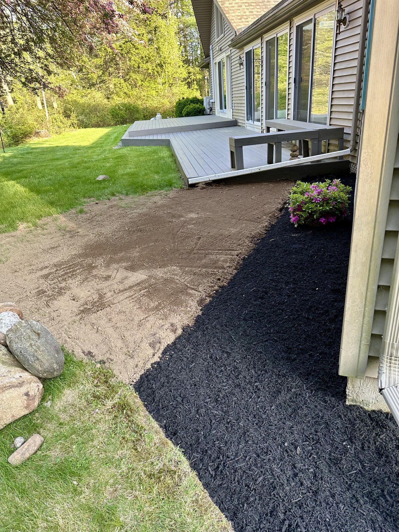 Fresh black mulch bed beside a composite deck with newly loamed ground alongside
