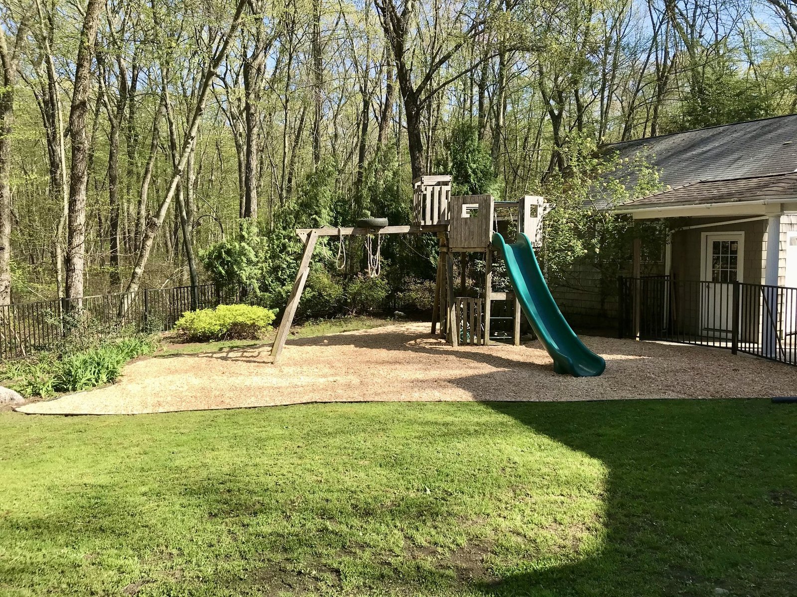 Wooden swing set on a fresh pea stone play area edged against a green backyard lawn